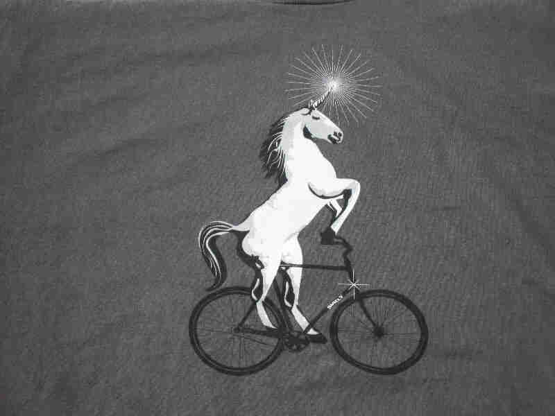 Front, chest area view of a gray Surly Bikes t-shirt with a graphic of unicorn riding a bike