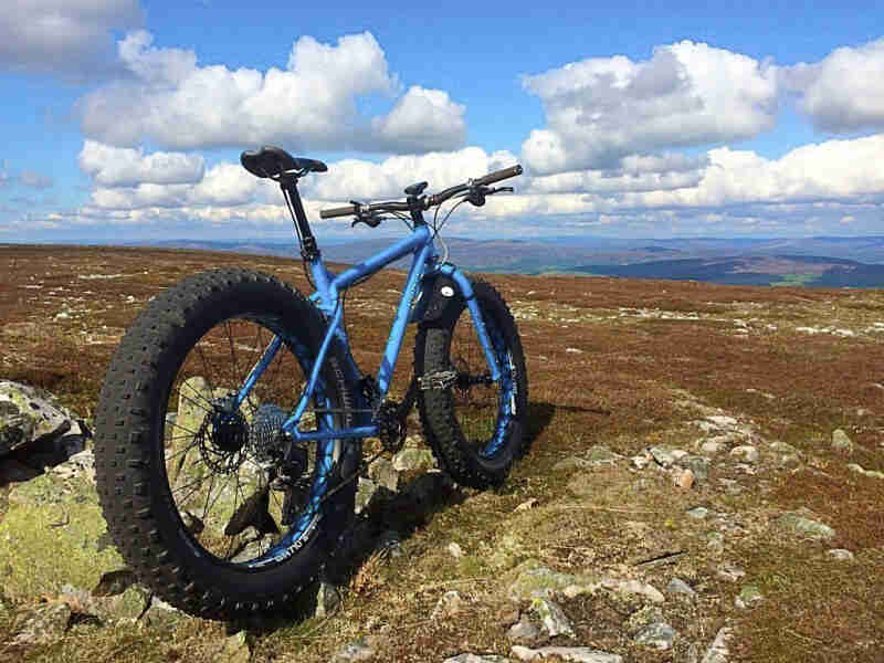 Rear view of a blue Surly fat parked on rocky field, with blue sky and white cloud above