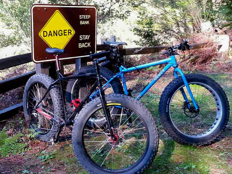 Front right view of 2 Surly Ice Cream Truck fat bikes, side by side, parked in front of Danger sign and a wood fence