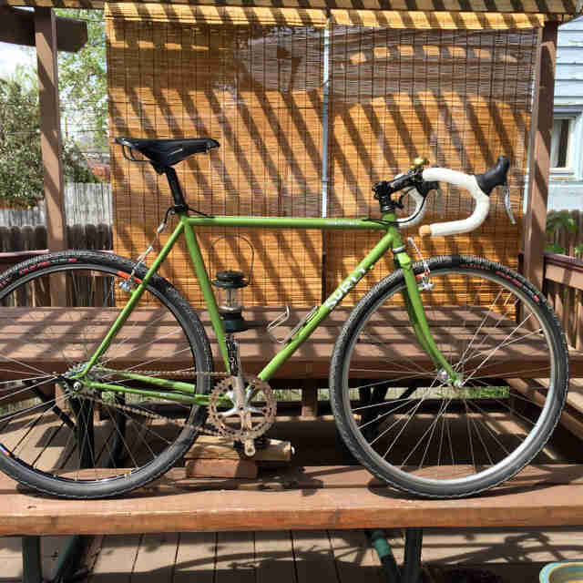 Right side view of a green Surly Cross Check bike, parked on a picnic table under a pergola