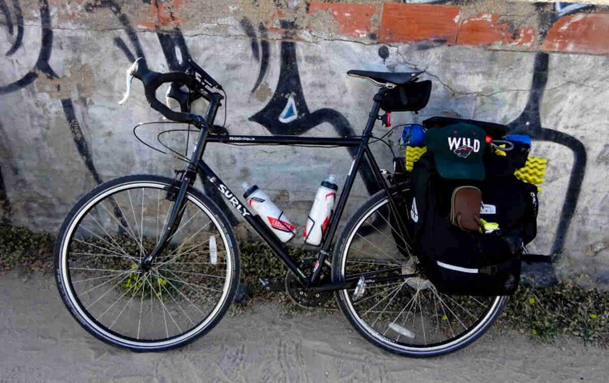 Left side view of a black Surly Cross Check bike, leaning on a wall with graffiti