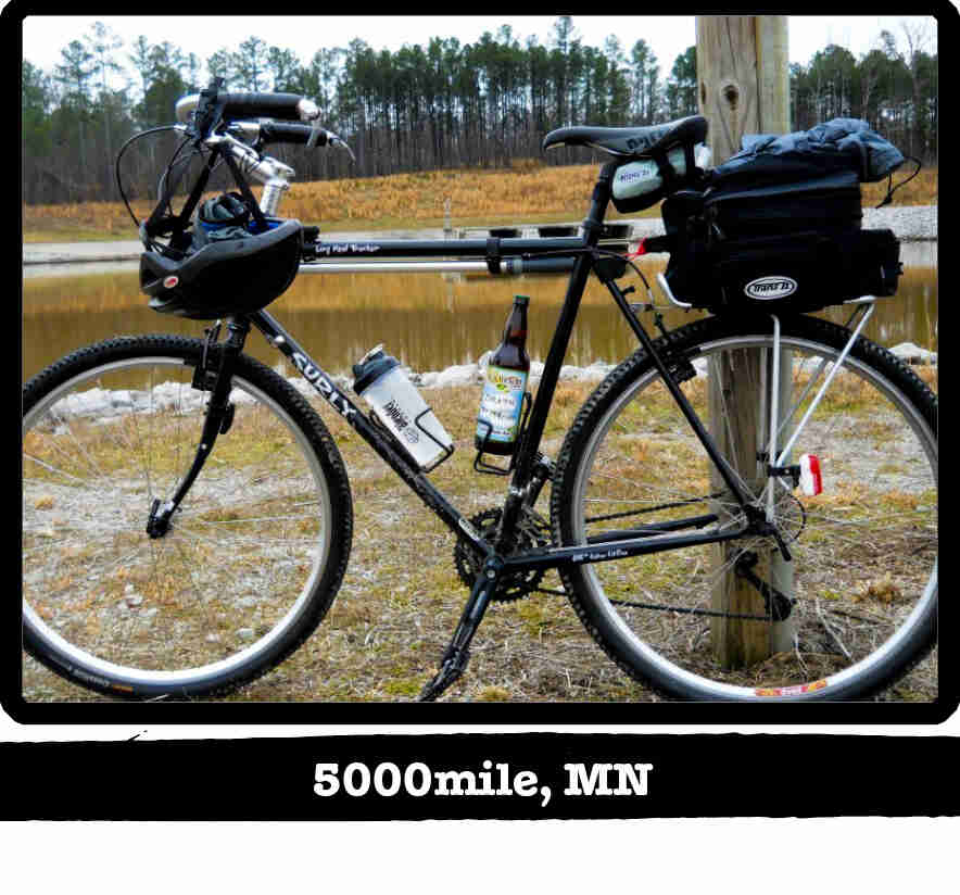 Left side view of a black Surly Long Haul Trucker bike with gear, in front of a pond - 5000mile, MN tag below image