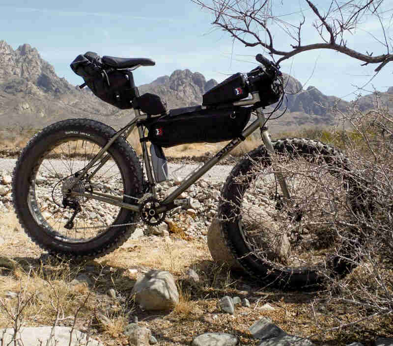 Right profile of a Surly fat bike, parked on rocks, with a mountain range in the background