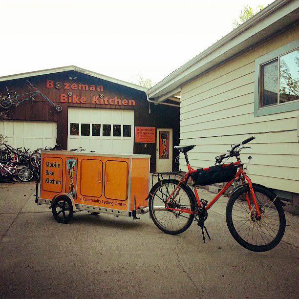 Right angled view of a Surly Troll bike with food trailer attached, in a driveway, with a garage in the background