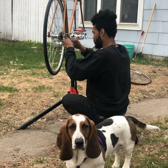 Cyclist squats down while fixing a drive chain on a bike with a basset hound